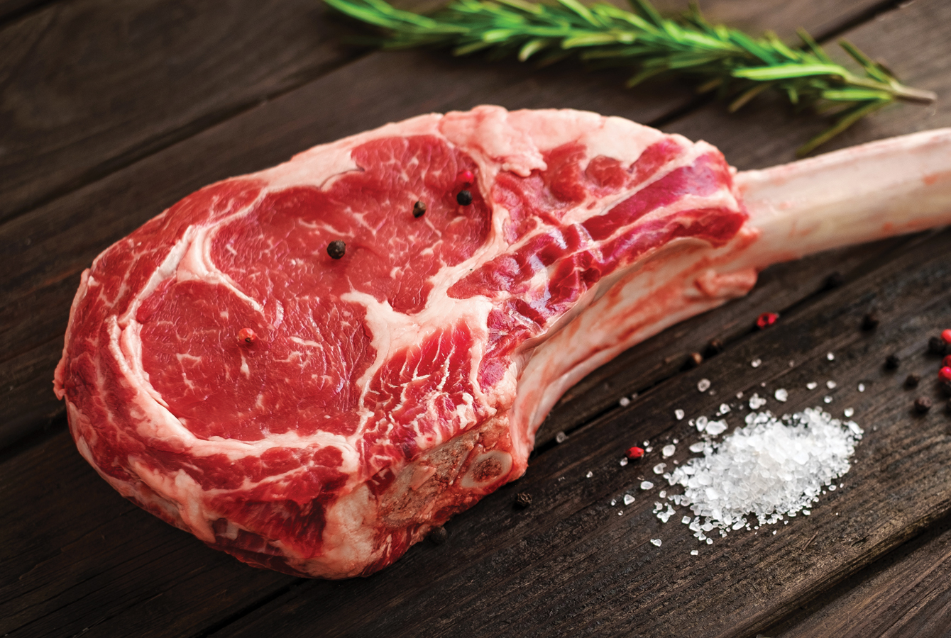 A raw Tomahawk steak on a shiny wooden surface, ready to be grilled.