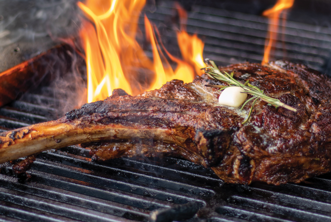A Tomahawk Steak on the grill, flames high and searing the meat beautifully.